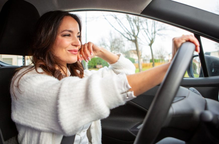 Smiling young woman enjoying a pleasant drive in her car on a bright day, looking confident and relaxed behind the wheel